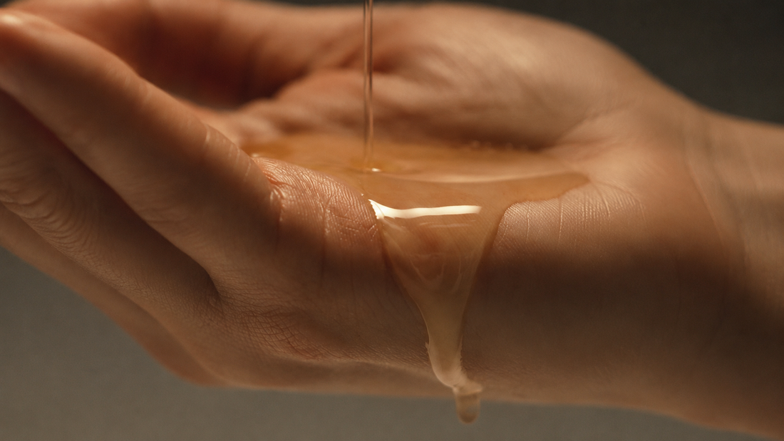 Golden body oil streams into an open palm, showing its smooth, lightweight texture.