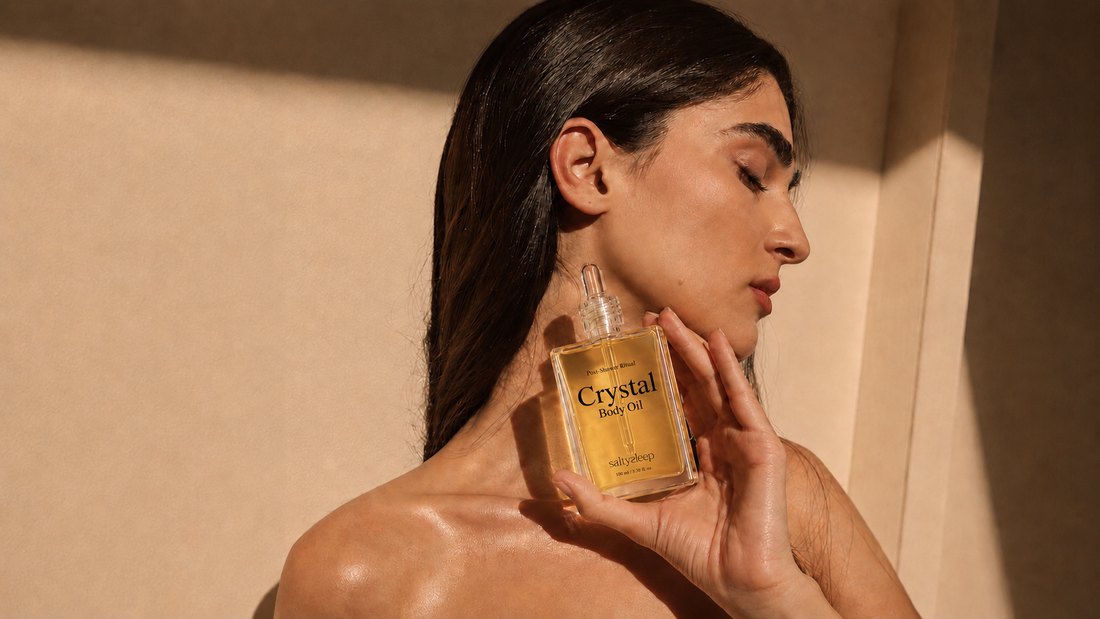 A woman holds Crystal Body Oil near her neck, wearing an earring, feeling the warm scent.