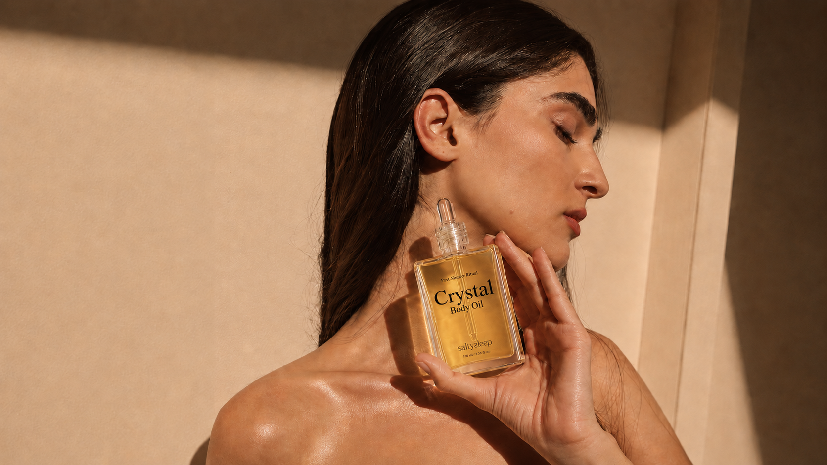 A woman holds Crystal Body Oil near her neck, wearing an earring, feeling the warm scent.